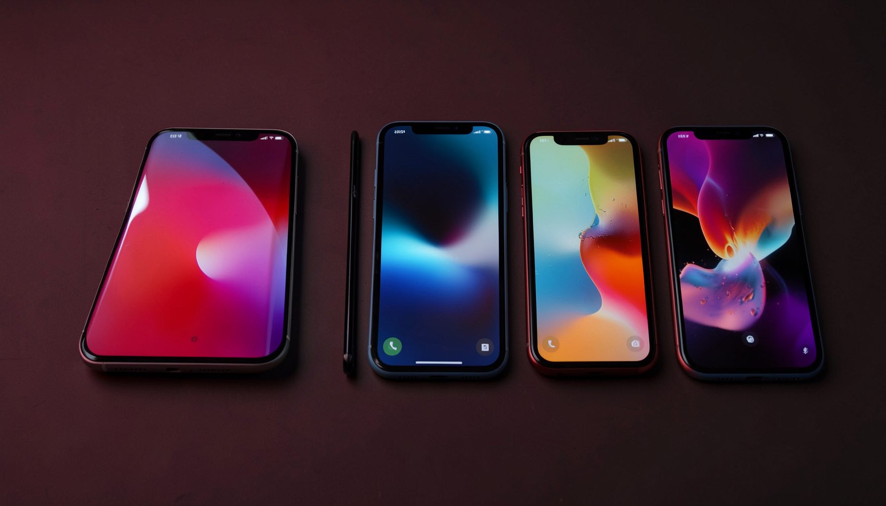 A row of modern smartphones with colorful displays arranged on a dark surface, deep red and charcoal tones dominating the scene