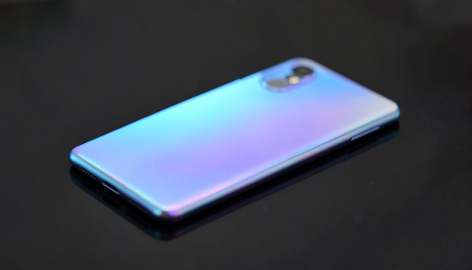 Smartphone with a gradient iridescent fuselage in soft blue and purple tones, resting on a dark reflective surface